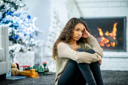 Woman stressing over holidays in front of fire and tree.